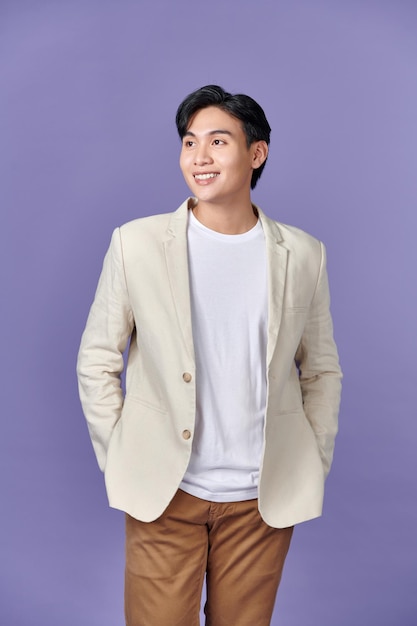 Sorridente jovem empresário asiático em terno bege isolado no fundo roxo