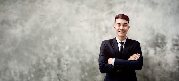 Sorridente jovem empresário de pé perto da parede de concreto do sotão. Braços cruzados e olhando para a câmera. mais espaço de cópia com tamanho grande