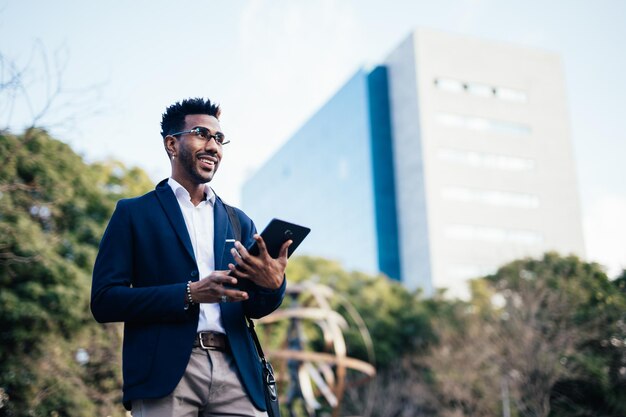 Sorridente jovem empresário negro usando um tablet em um parque no centro da cidade