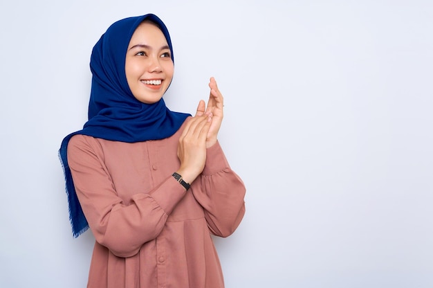 Sorridente jovem muçulmana asiática de camisa rosa esfrega as mãos se sente alegre tem dentes brancos isolados sobre fundo branco Conceito de estilo de vida religioso de pessoas