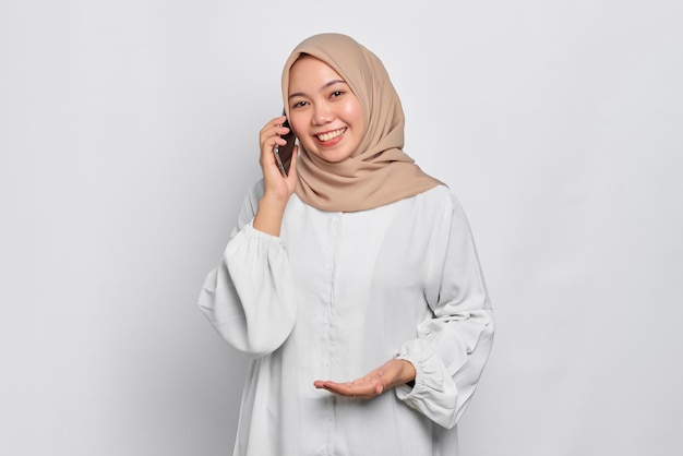 Sorridente jovem muçulmana asiática falando no celular isolado sobre fundo branco