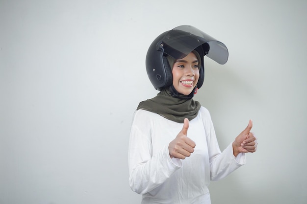 Sorridente jovem muçulmana asiática mostrando os dois polegares para cima usando capacete de motocicleta