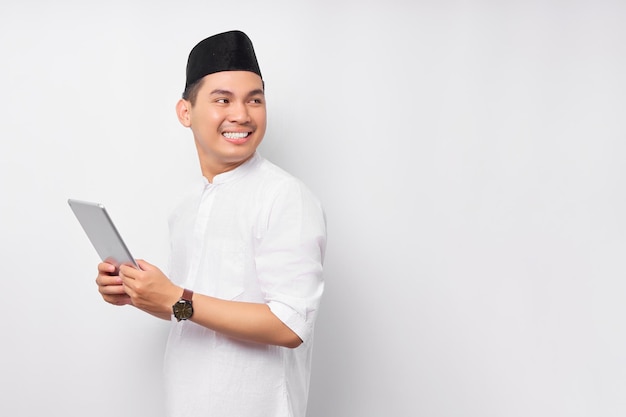 Sorridente jovem muçulmano asiático segurando tablet digital e olhando para o espaço de cópia vazio isolado no fundo branco Celebração do conceito de estilo de vida religioso do Islã de pessoas Ramadã e Ied Mubarak