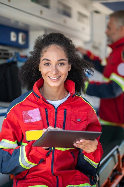 Foto sorridente jovem paramédico com o computador tablet nas mãos, sentado no carro da ambulância