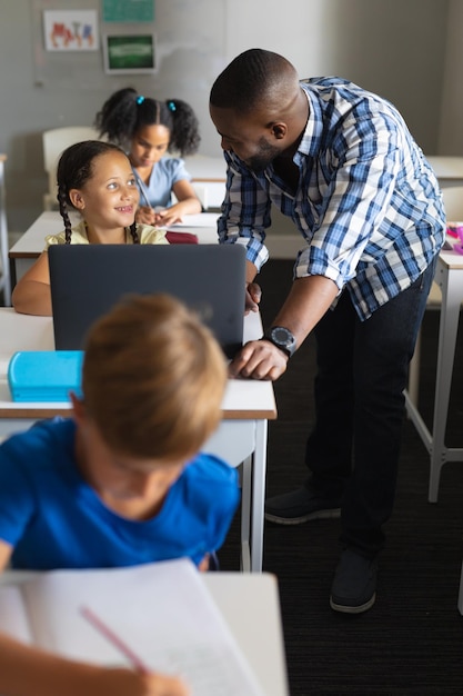 Sorridente jovem professor afro-americano olhando para uma colegial caucasiana com laptop