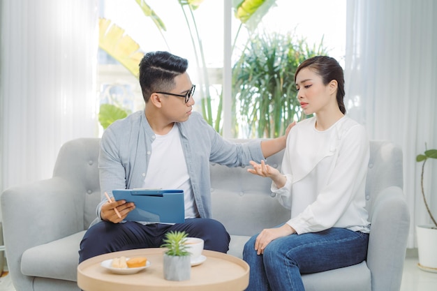 Sorridente jovem psiquiatra masculino asiático conversando com uma jovem em seu escritório