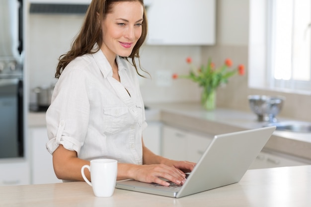 Sorridente jovem usando laptop na cozinha