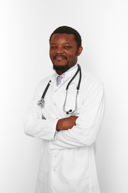 Sorridente médico barbudo preto cruzou os braços em roupão branco com fundo branco estetoscópio