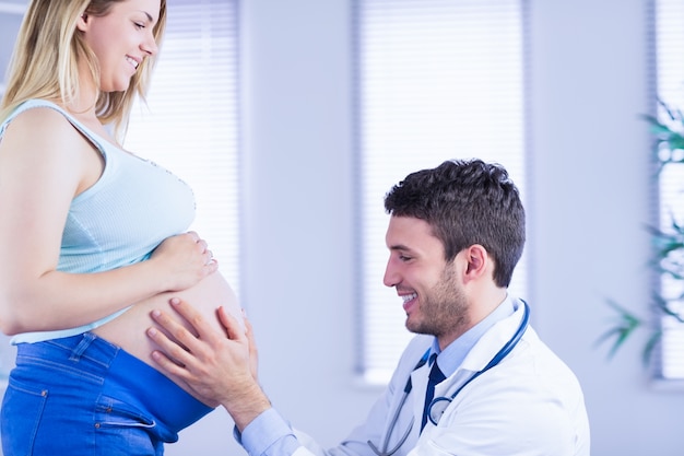 Sorridente médico verificando o estômago de uma paciente grávida