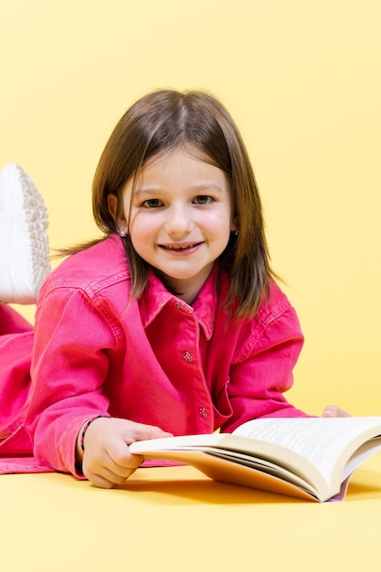 Sorridente menina bonitinha segurando um livro e olhando direto para a câmera