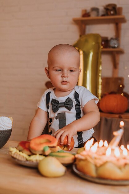 Sorridente menino de um ano de idade em roupas festivas tem uma maçã nas mãos. primeiro aniversário. corpo com o número um. bola de folha dourada. lanche saudável para crianças. pequeno cozinheiro. Foto de alta qualidade