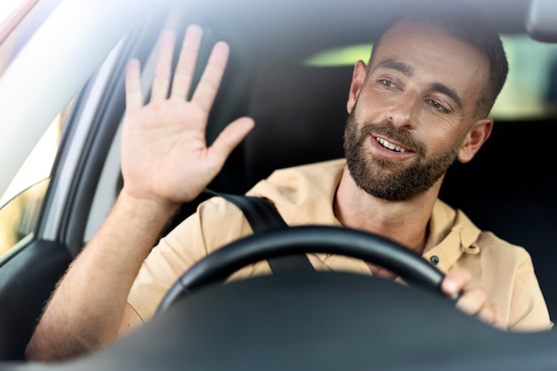 Foto sorridente motorista de táxi latino acenando com a mão esperando o cliente sentado no carro. conceito de transporte