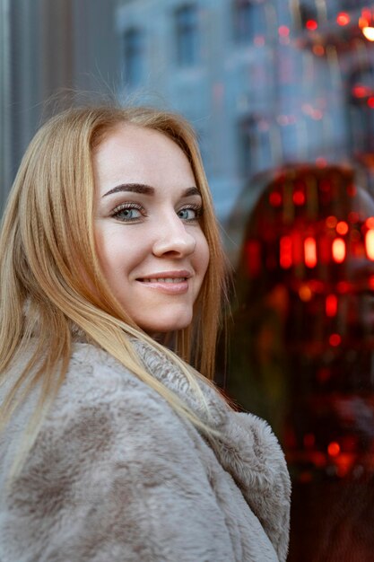 Sorridente mulher atraente de olhos azuis contra o fundo de uma janela de loja vermelha Fim de semana de férias ao ar livre Quadro vertical