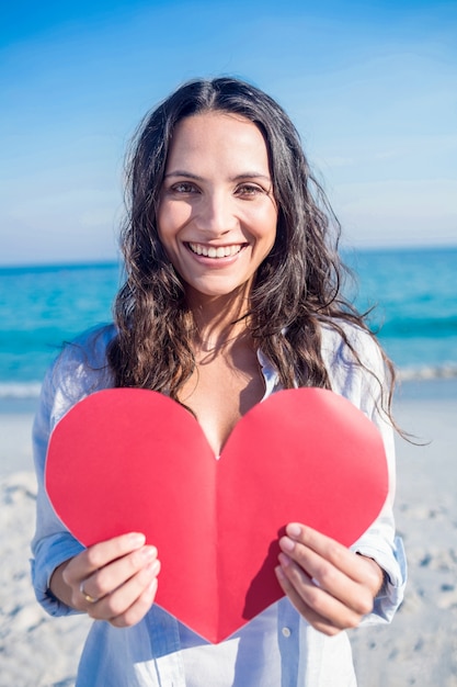 Sorridente mulher segurando cartão de coração na praia