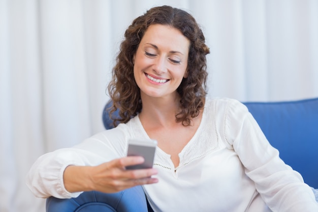 Sorridente mulher sentada no sofá e usando seu smartphone