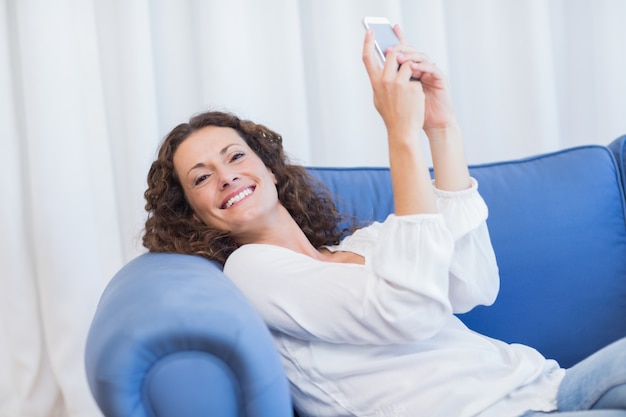 Sorridente mulher sentada no sofá e usando seu smartphone
