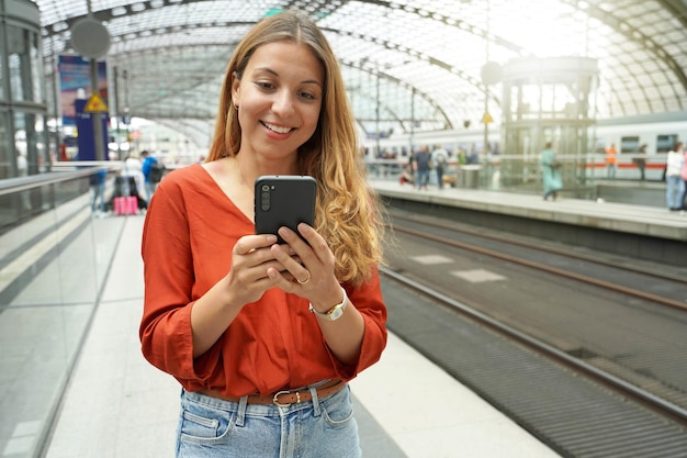 Sorridente passageiro viajante brasileiro atraente compra passagem on-line com smartphone na estação de trem Copiar espaço