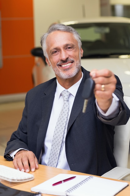 Sorridente vendedor que dá chaves de carro de um cliente