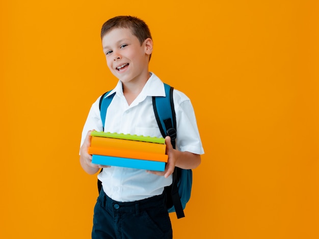 Sorrindo alegre estudante contra fundo amarelo. Uma criança com mochila, livros e cadernos.