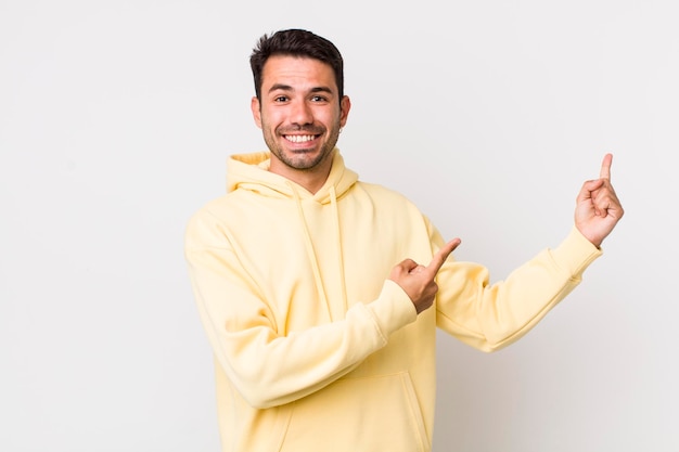 Sorrindo alegremente e apontando para o lado e para cima com as duas mãos, mostrando o objeto no espaço da cópia