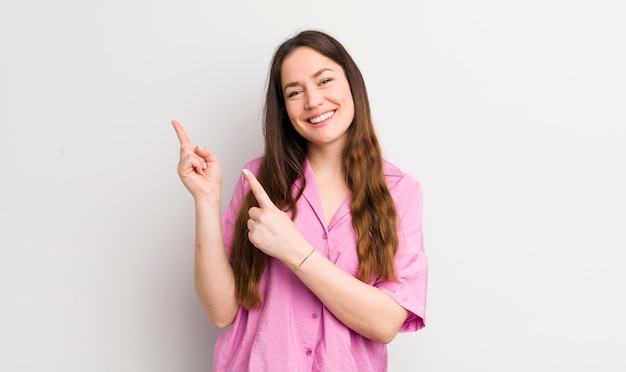 Sorrindo alegremente e apontando para o lado e para cima com as duas mãos, mostrando o objeto no espaço da cópia