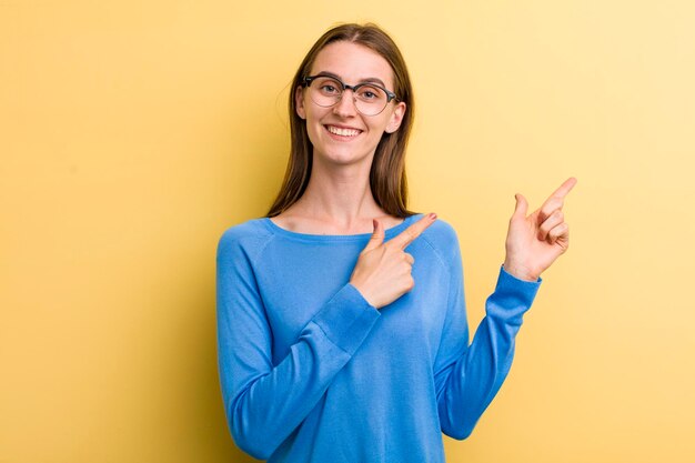 Sorrindo alegremente e apontando para o lado e para cima com as duas mãos, mostrando o objeto no espaço da cópia