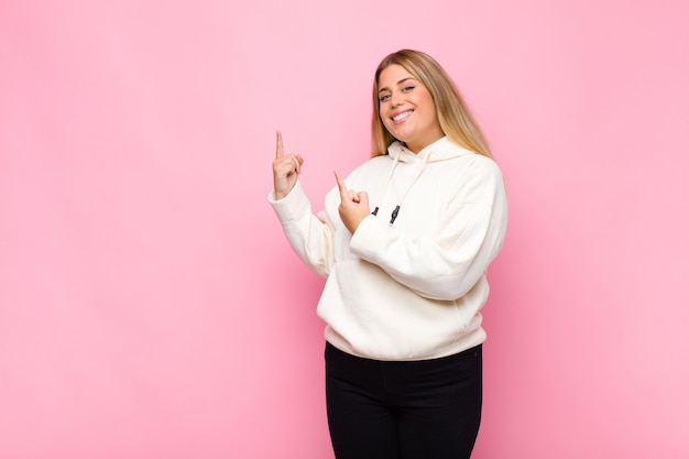 Sorrindo alegremente e apontando para o lado e para cima com as duas mãos, mostrando o objeto no espaço da cópia