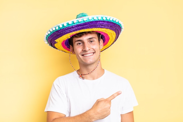 Sorrindo alegremente, sentindo-se feliz e apontando para o lado e para cima, mostrando o objeto no conceito de chapéu mexicano de espaço de cópia