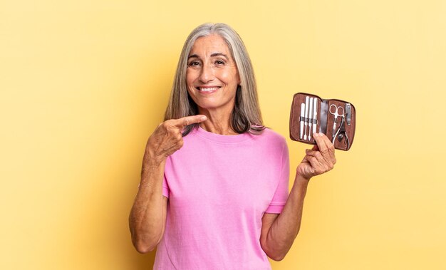 Foto sorrindo alegremente, sentindo-se feliz e apontando para o lado e para cima, mostrando o objeto no espaço da cópia, segurando um estojo de ferramentas de unhas