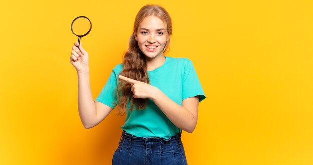 sorrindo alegremente, sentindo-se feliz e apontando para o lado e para cima, mostrando o objeto no espaço da cópia