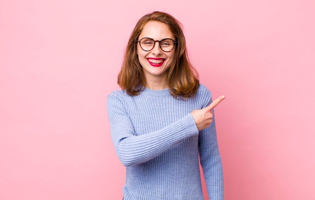 sorrindo alegremente sentindo-se feliz e apontando para o lado e para cima mostrando o objeto no espaço da cópia