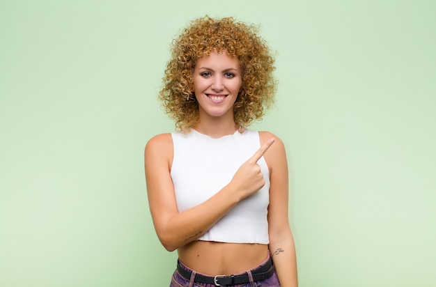 sorrindo alegremente, sentindo-se feliz e apontando para o lado e para cima, mostrando o objeto no espaço da cópia