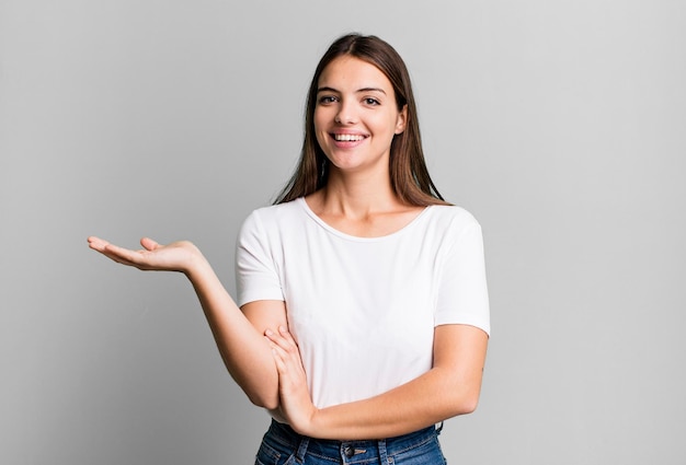 sorrindo alegremente, sentindo-se feliz e mostrando um conceito no espaço da cópia com a palma da mão