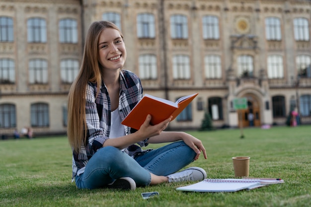 Sorrindo aluno estudando, lendo um livro, aprendendo a língua, preparação para o exame, sentado na grama, conceito de educação