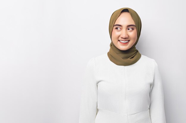 Sorrindo amigável jovem bela mulher muçulmana asiática 20 anos usando hijab olhando para o espaço vazio com expressão facial feliz isolada no fundo branco Conceito de estilo de vida religioso de pessoas