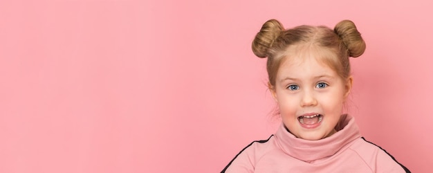 Sorrindo animada e feliz menina engraçada usando coques de cabelo fechando o retrato no fundo rosa