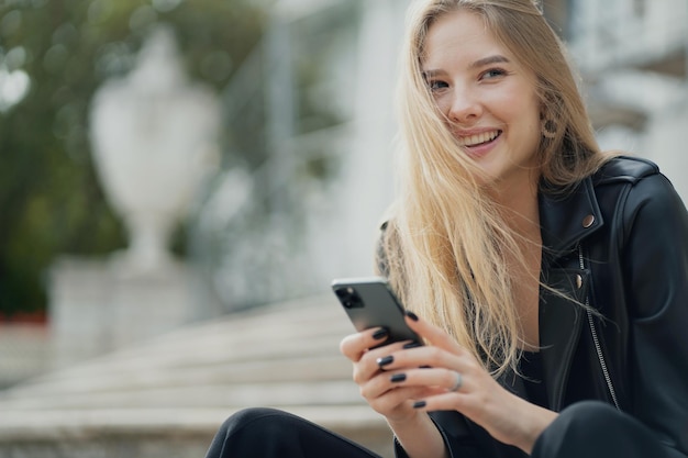 Sorrindo belo retrato de uma jovem segurando o telefone nas mãos mandando mensagens de texto