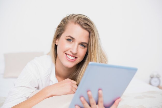 Sorrindo bonito modelo usando seu tablet pc deitado na cama aconchegante