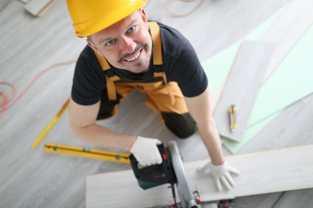 Sorrindo carpinteiro capacete serrar piso laminado