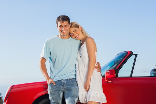 Sorrindo casal bonito posando contra o seu cabriolet vermelho