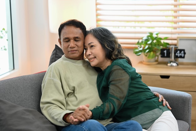 Sorrindo casal sênior de mãos dadas enquanto sentados juntos sofá confortável conceito de seguro de saúde de estilo de vida de aposentadoria