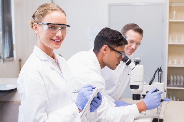 Sorrindo cientista olhando câmera enquanto colegas trabalhando com microscópio