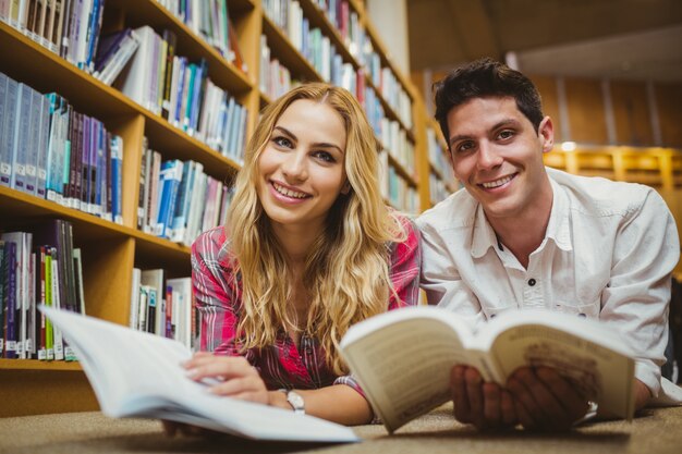 Sorrindo, colegas, leitura, livro, enquanto, inclinar-se, estantes de livros, em, biblioteca