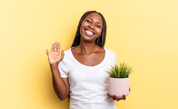 Sorrindo com alegria e alegria, acenando com a mão, dando as boas-vindas e cumprimentando ou dizendo adeus segurando um vaso de plantas