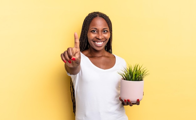 Sorrindo com orgulho e confiança fazendo a pose número um de forma triunfante, sentindo-se como um líder segurando um vaso de plantas