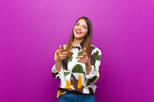 sorrindo com uma atitude positiva, bem-sucedida e feliz, apontando para a câmera, fazendo sinal de arma com as mãos