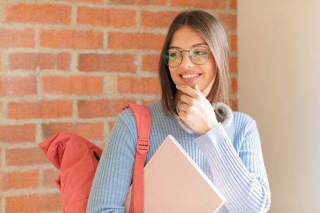 Sorrindo com uma expressão feliz e confiante com a mão no queixo, pensando e olhando para o lado