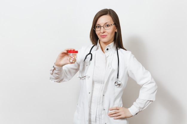 Sorrindo confiante linda jovem médica com estetoscópio, óculos isolados no fundo branco. Médica em vestido de médico segura o frasco com comprimidos. Pessoal de saúde, conceito de medicina.