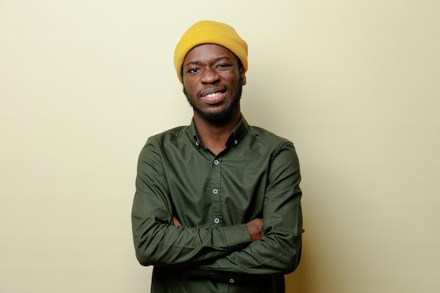 Sorrindo cruzando as mãos jovem afro-americano de chapéu vestindo camisa verde isolada em fundo branco