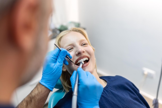 Sorrindo dentista se comunicando com jovem enquanto verificava os dentes durante o procedimento odontológico no consultório do dentista